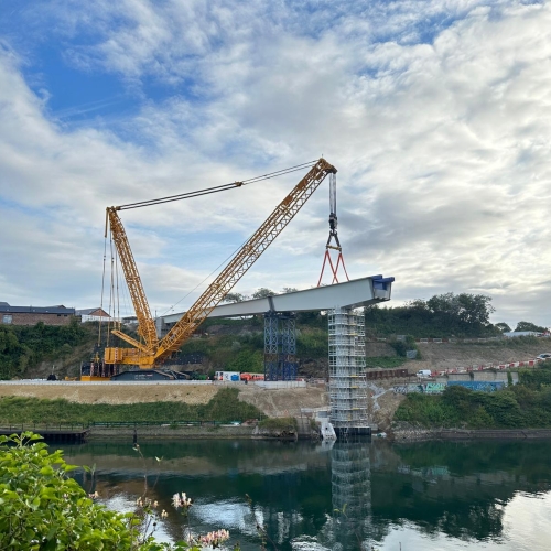 Crane lifting a section of the bridge into place on a sunny day.