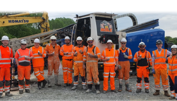 Photo of 12 people in orange PPE stood smiling at the camera